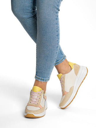 Beige sneakers with yellow accents worn with blue jeans on a white background
