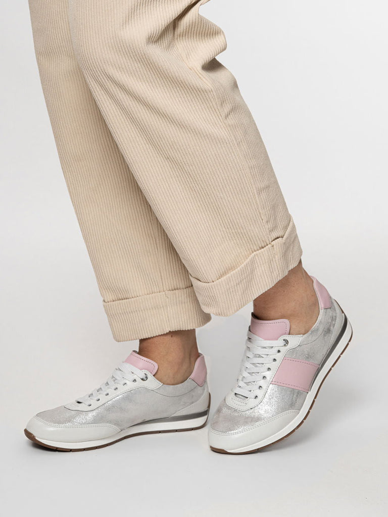 silver sneakers with pink accents worn with beige pants on a white background