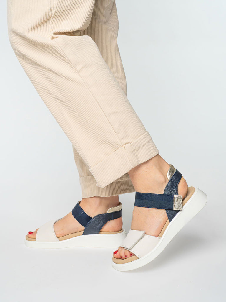Navy sandals worn with beige pants on a light gray background