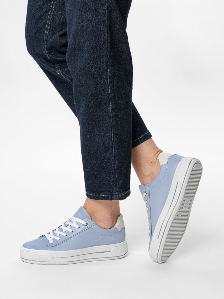 Light blue sneakers worn with dark jeans on a white background