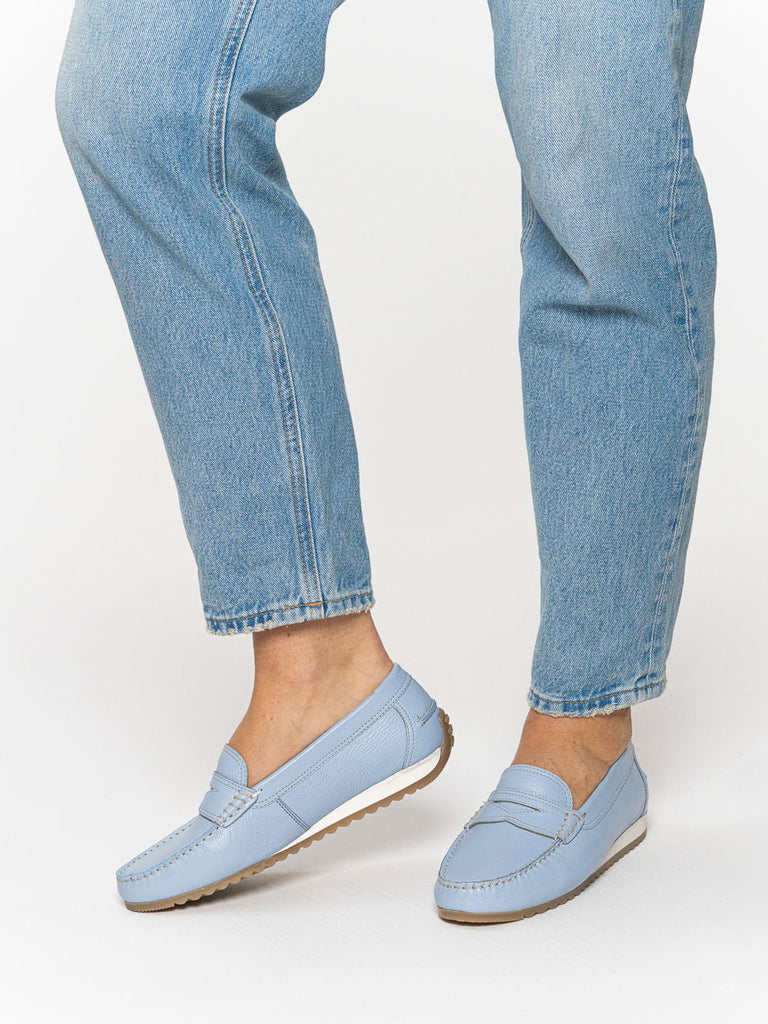 Light blue loafers worn with light blue jeans on a white background