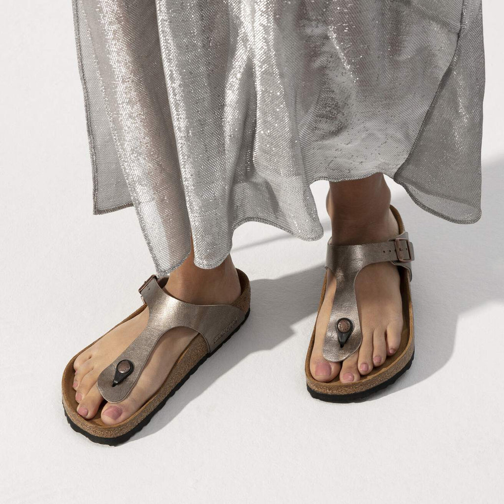 Person wearing metallic sandals with a plain background