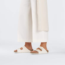 Load image into Gallery viewer, Person wearing white sandals with brown straps on a plain background
