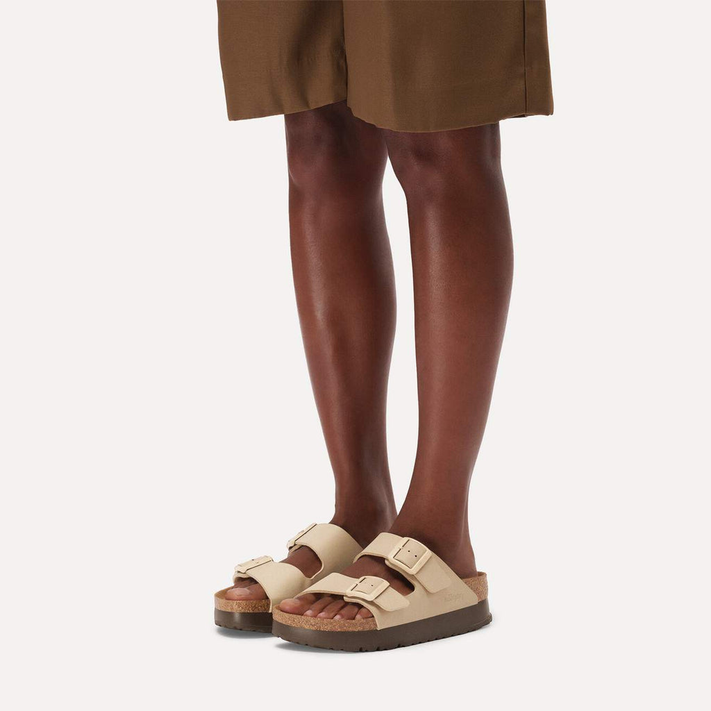 Beige sandals worn with brown shorts on a white background