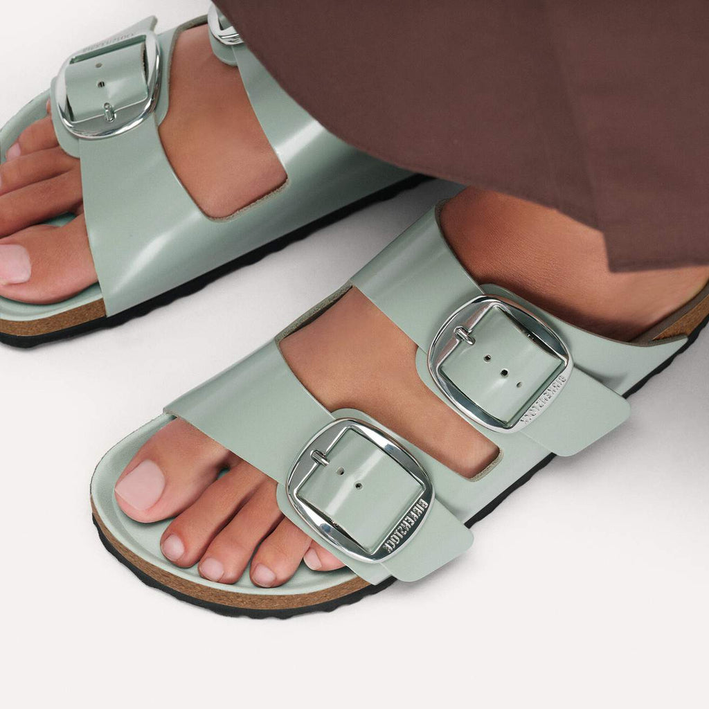 Light green sandals with silver buckles worn by a person on a white background