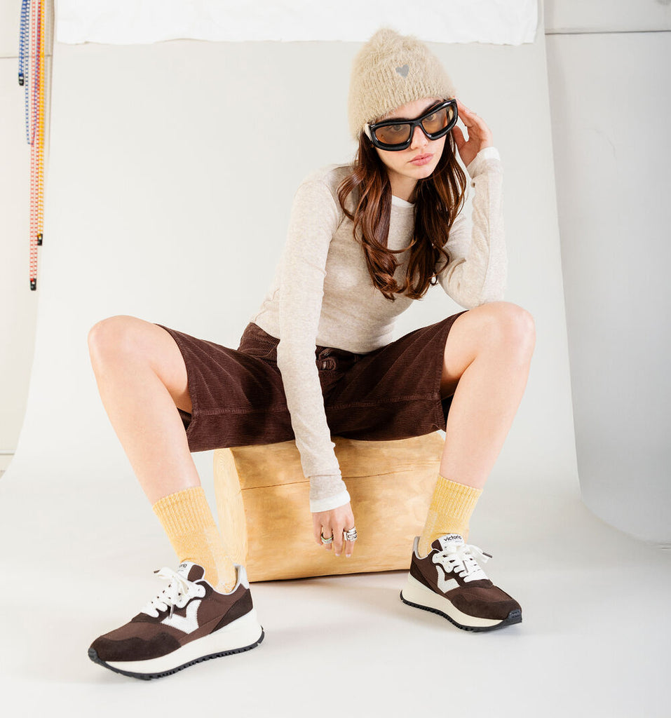 Person sitting on a bean bag chair wearing a white sweater, brown shorts, and brown sneakers.