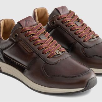A dark brown leather sneaker with matching brown laces, a black textured heel panel, and a white midsole, shown in a side profile on a white background.