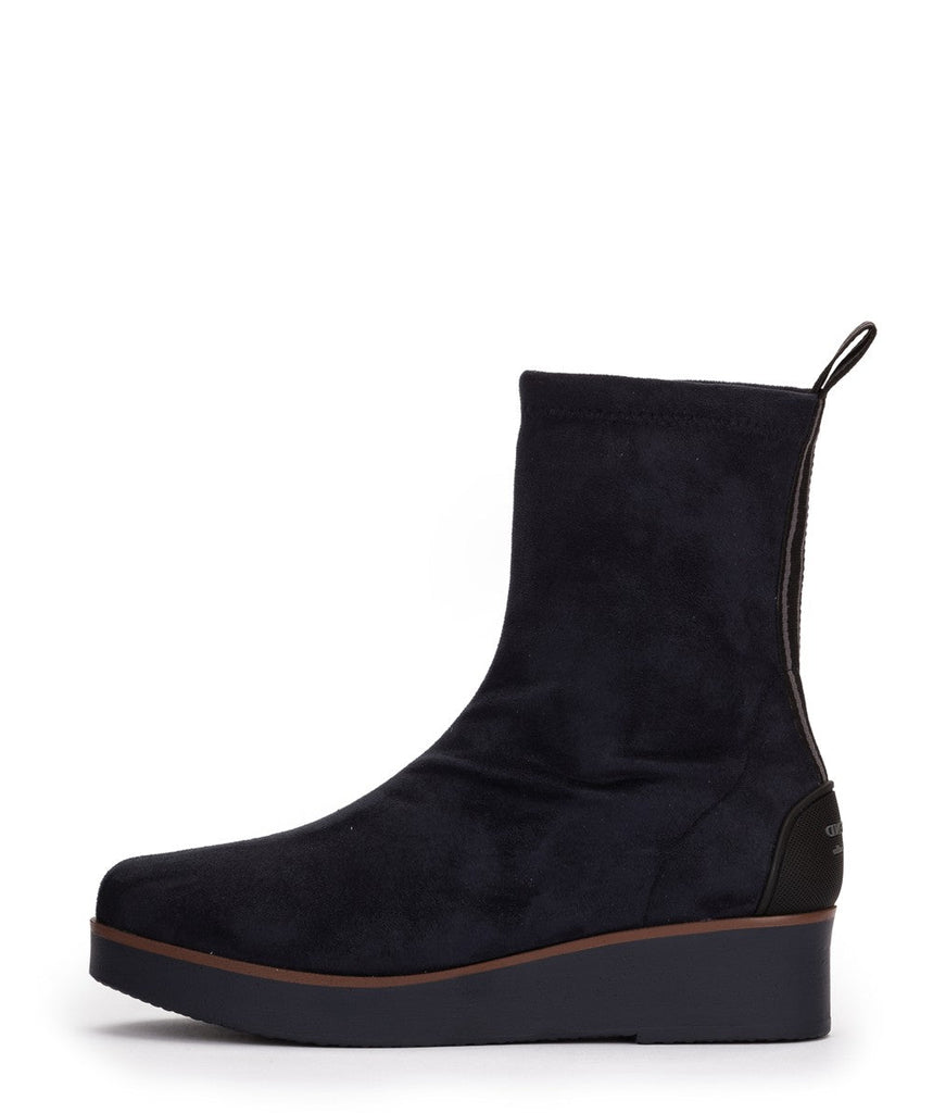 A dark navy blue suede ankle boot with a thick platform wedge heel, a brown midsole accent, and a small pull tab at the heel, shown from a side profile on a white background.