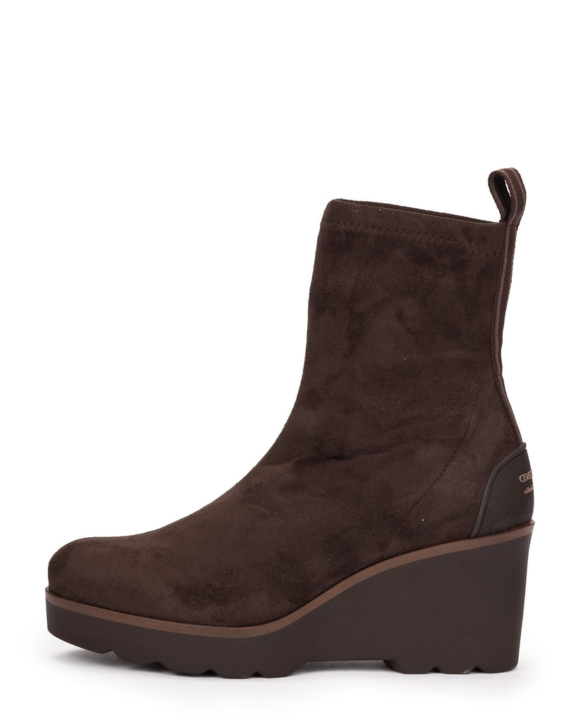 A dark brown suede ankle boot with a chunky wedge heel and a small pull tab at the back, shown from a side profile on a white background.