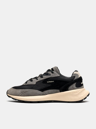 A low-top sneaker in black and gray suede and mesh, featuring a thick beige midsole and the brand name 'HOEF' printed on the side, set against a light gray background.