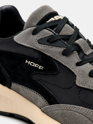 A low-top sneaker in black and gray suede and mesh, featuring a thick beige midsole and the brand name 'HOEF' printed on the side, set against a light gray background.