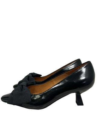 A pair of black pointed-toe pumps with a wide fabric bow detail across the vamp and a low kitten heel, shown against a plain light gray background.