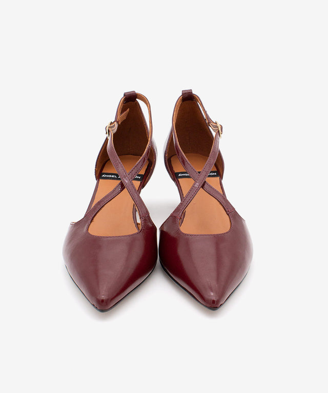 Pair of maroon pointed-toe shoes with criss-cross straps on a white background