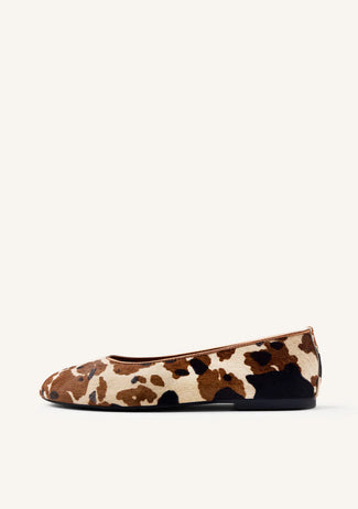 Pair of cow print flats on a white background