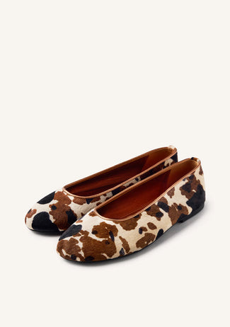 Pair of cow print flats on a white background