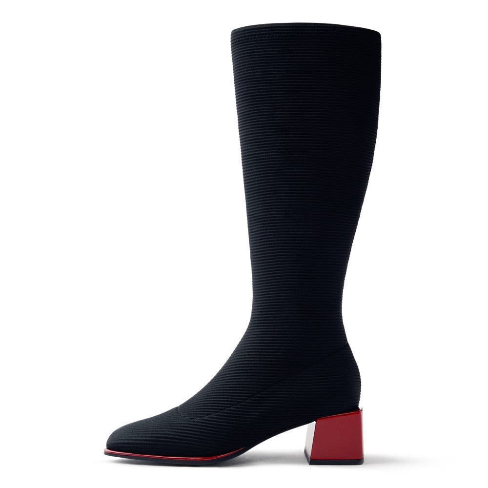 A single knee-high ribbed boot in black with a contrasting red block heel and red outsole edge, shown in profile against a white background.