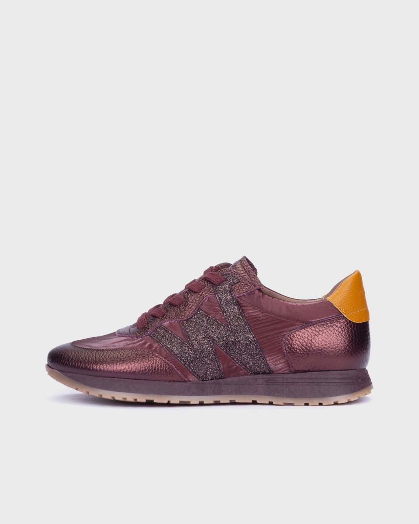 A low-top sneaker in metallic burgundy with a textured glittery side stripe, a bright yellow heel tab, and a beige gum sole, shown from a side profile on a light gray background.