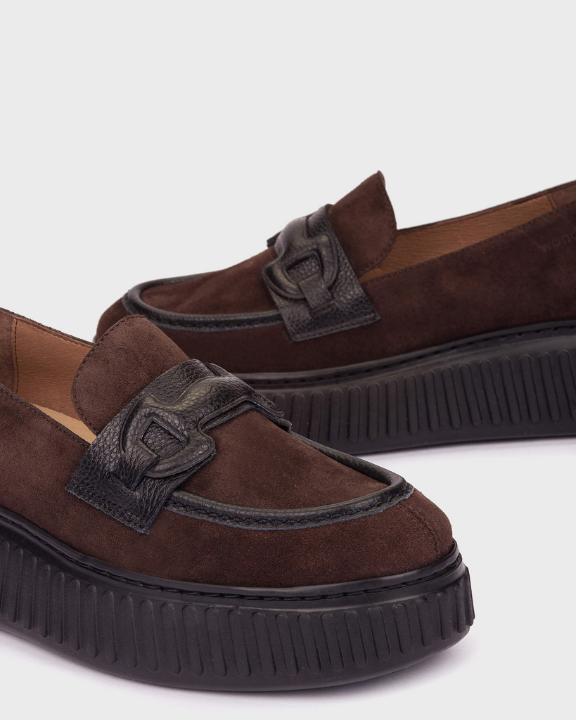 A pair of dark brown suede platform loafers with black faux-leather strap details and thick black platform soles, shown on a light gray background.