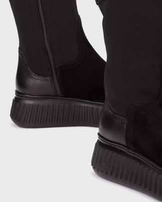 A black ankle boot with a matte black fabric upper, a glossy black cap toe, and a chunky black platform sole, shown in a side profile on a light gray background.