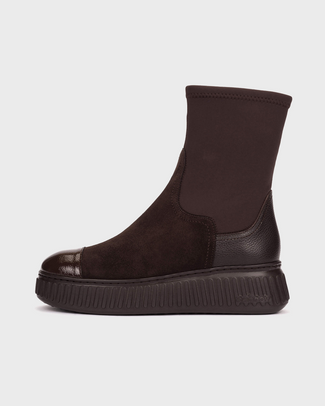 A dark brown ankle boot with a textured elastic side panel, a glossy leather toe cap, and a chunky ribbed platform sole, shown from a side profile on a light gray background.