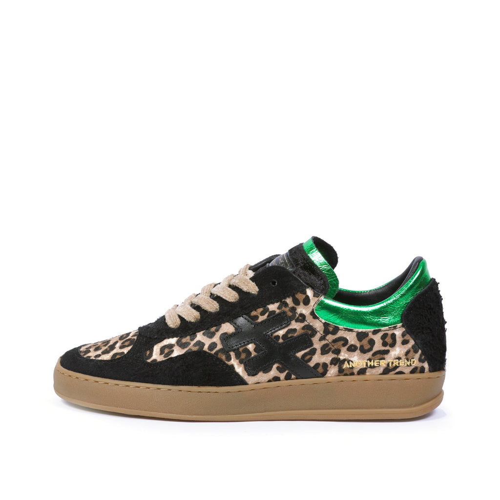 A low-top sneaker featuring a black suede base with a beige and black leopard print pattern on the toe box, black side panels, beige laces, a metallic green collar, and a gum brown sole.