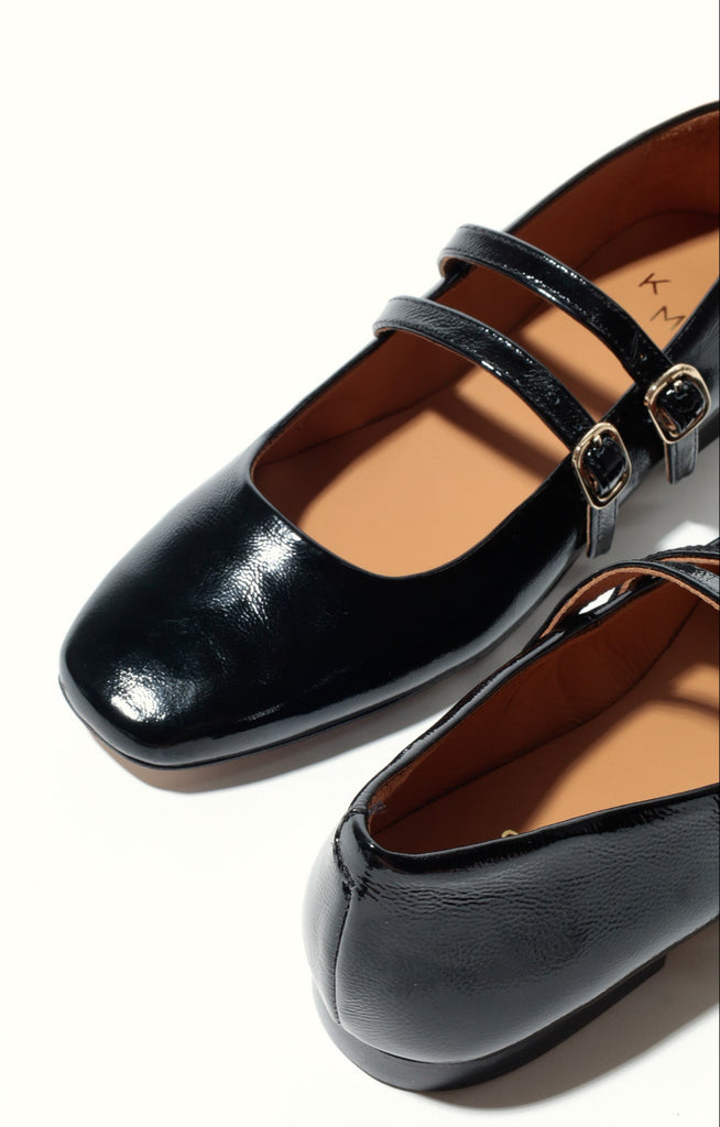 Black patent leather shoes with a strap on a white background