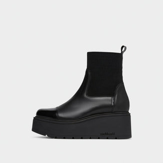 A black platform Chelsea boot with a ribbed knit ankle cuff, shown in a side profile against a light gray background.