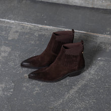 Load image into Gallery viewer, A pair of dark brown suede ankle boots with elastic side panels and pointed toes, displayed on a textured gray concrete floor.
