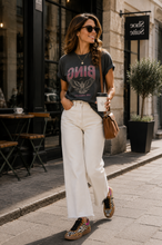 Load image into Gallery viewer, A woman walking on a city sidewalk wearing a dark gray graphic t-shirt with 'BING' in pink, white wide-leg cropped pants, and leopard-print sneakers, carrying a brown shoulder bag and holding a coffee cup.
