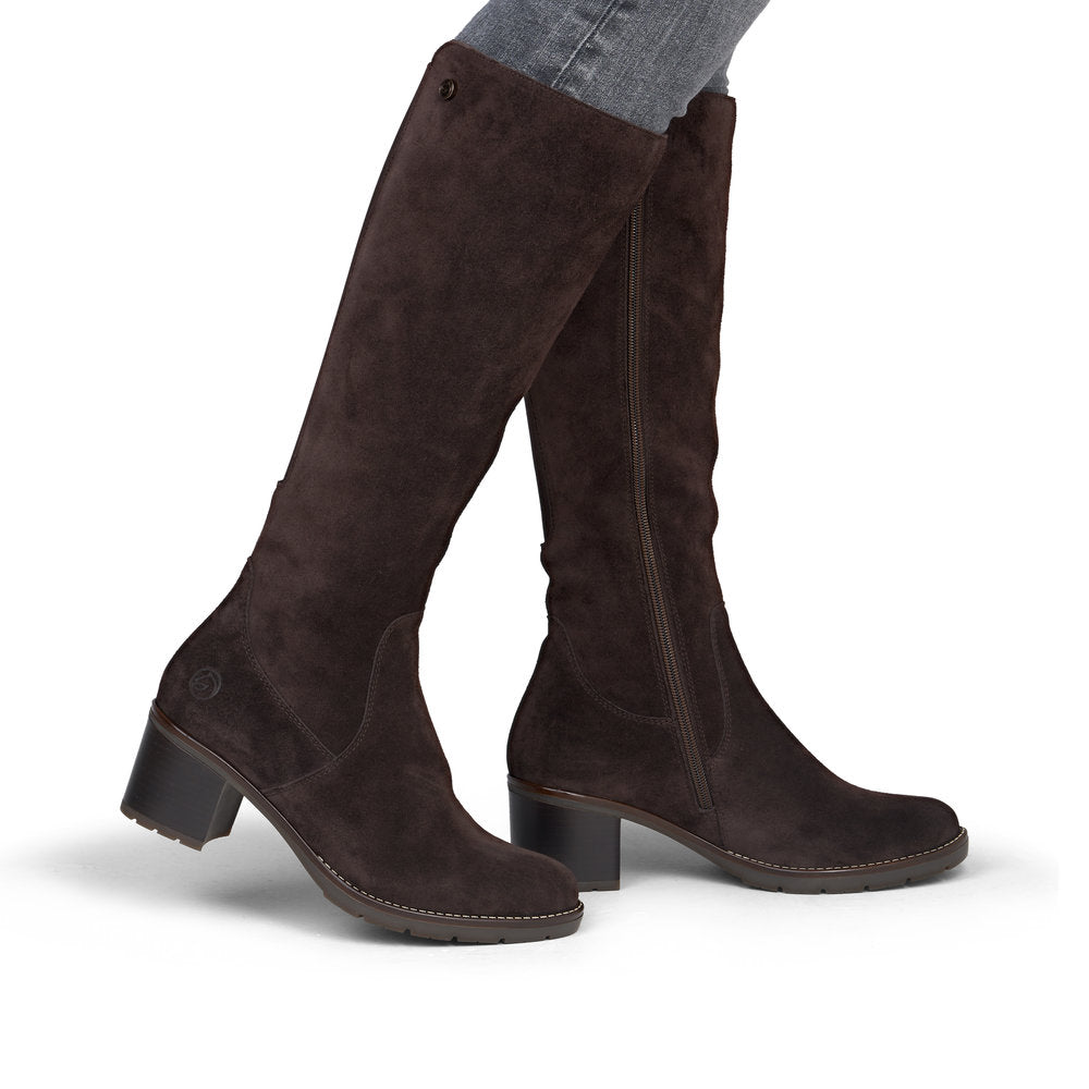 A pair of dark brown suede knee-high boots with low block heels, shown on a model's legs against a white background.