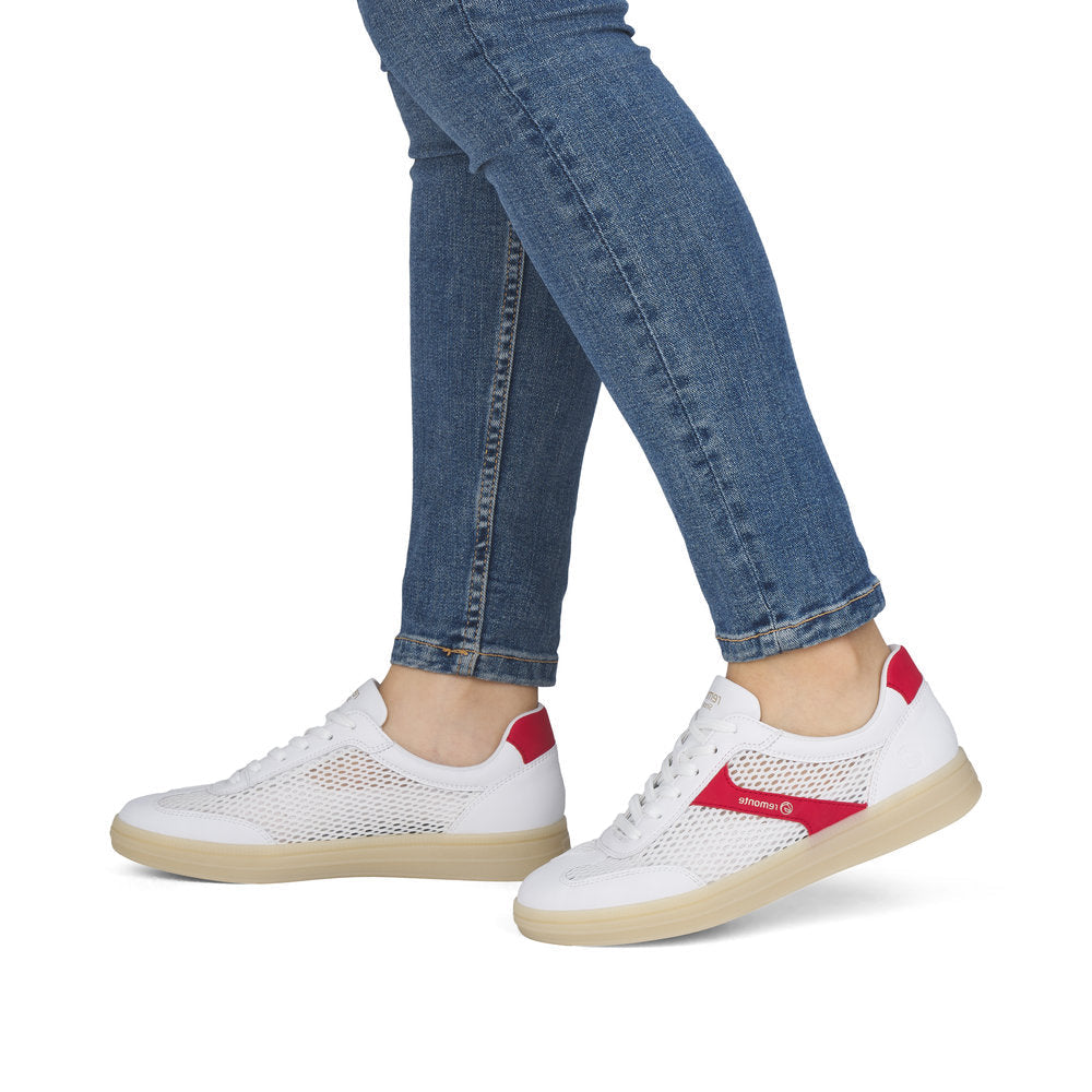 White sneakers with red accents worn with blue jeans on a white background
