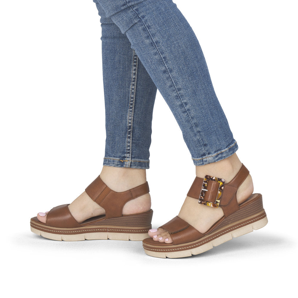 Brown sandals worn with blue jeans on a white background
