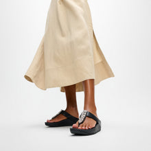 Load image into Gallery viewer, Black sandals with embellishments worn with a beige skirt on a white background
