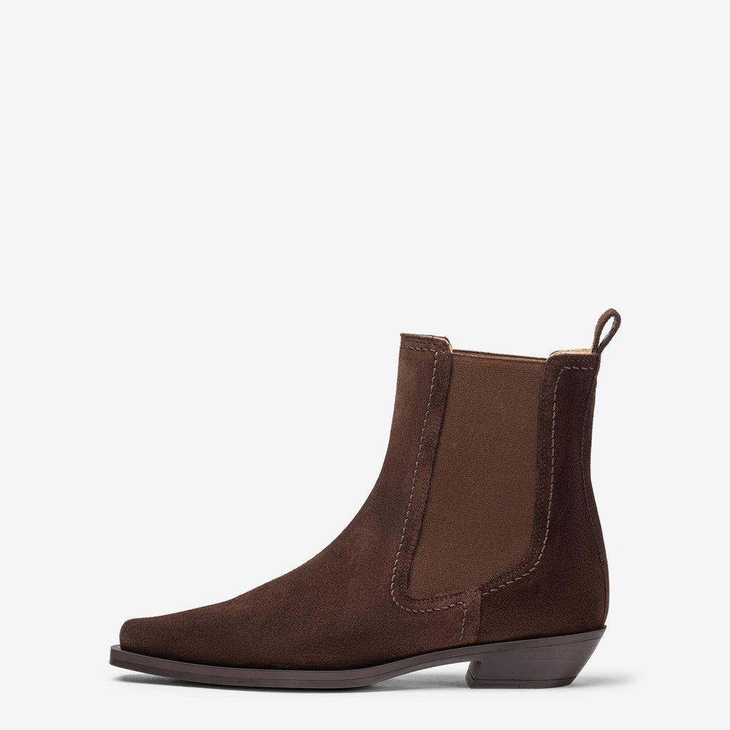 A dark brown suede Chelsea boot with a low block heel and elastic side gore, shown in profile against a light gray background.