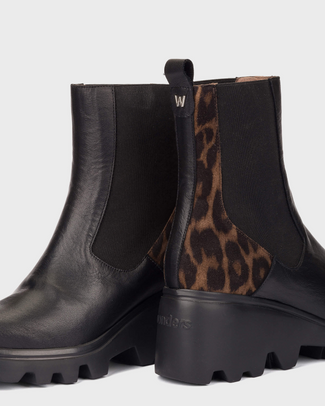 A black leather Chelsea-style ankle boot with a brown and black leopard print side panel, a black elastic side gore, and a chunky lug sole, shown against a light gray background.