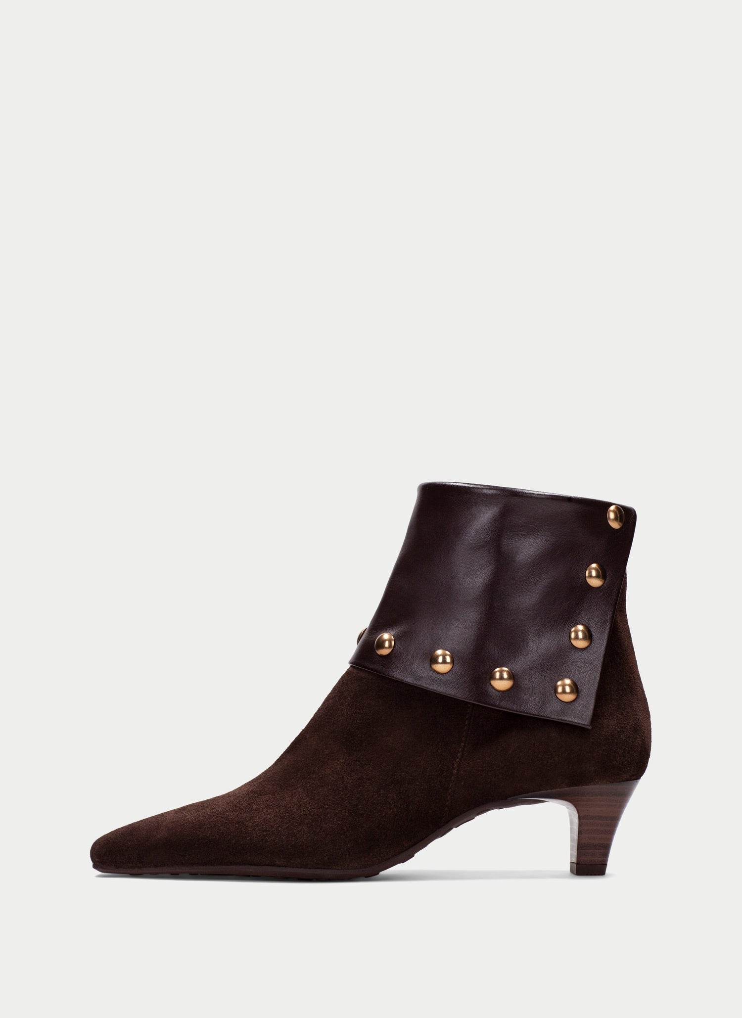 A dark brown suede ankle boot with a pointed toe, a low block heel, and decorative gold-tone metal studs on a matching faux-leather wrap around the collar, shown against a light gray background.