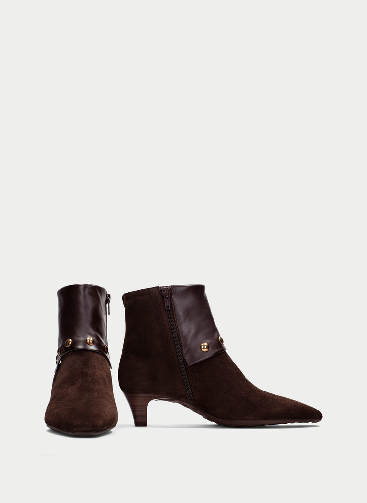 A pair of dark brown suede ankle boots with pointed toes, low kitten heels, and gold-tone hardware details, shown against a light gray background.