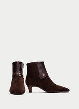 Load image into Gallery viewer, A pair of dark brown suede ankle boots with pointed toes, low kitten heels, and gold-tone hardware details, shown against a light gray background.

