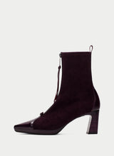 Load image into Gallery viewer, A dark plum purple suede ankle boot with a glossy patent leather toe cap and a block heel, shown from a side profile on a light gray background.

