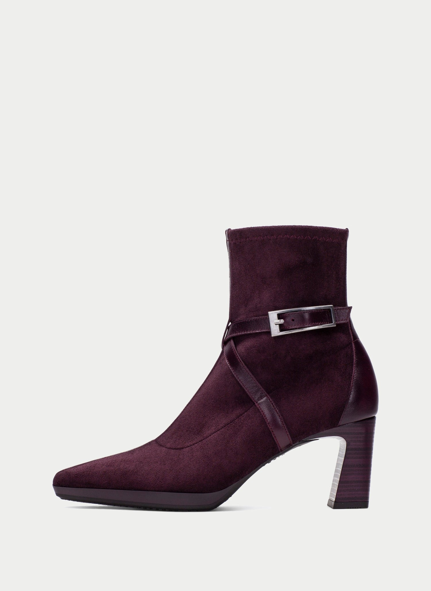 A dark plum purple suede ankle boot with a block heel, pointed toe, and a decorative strap with a silver buckle detail around the ankle, shown against a light gray background.