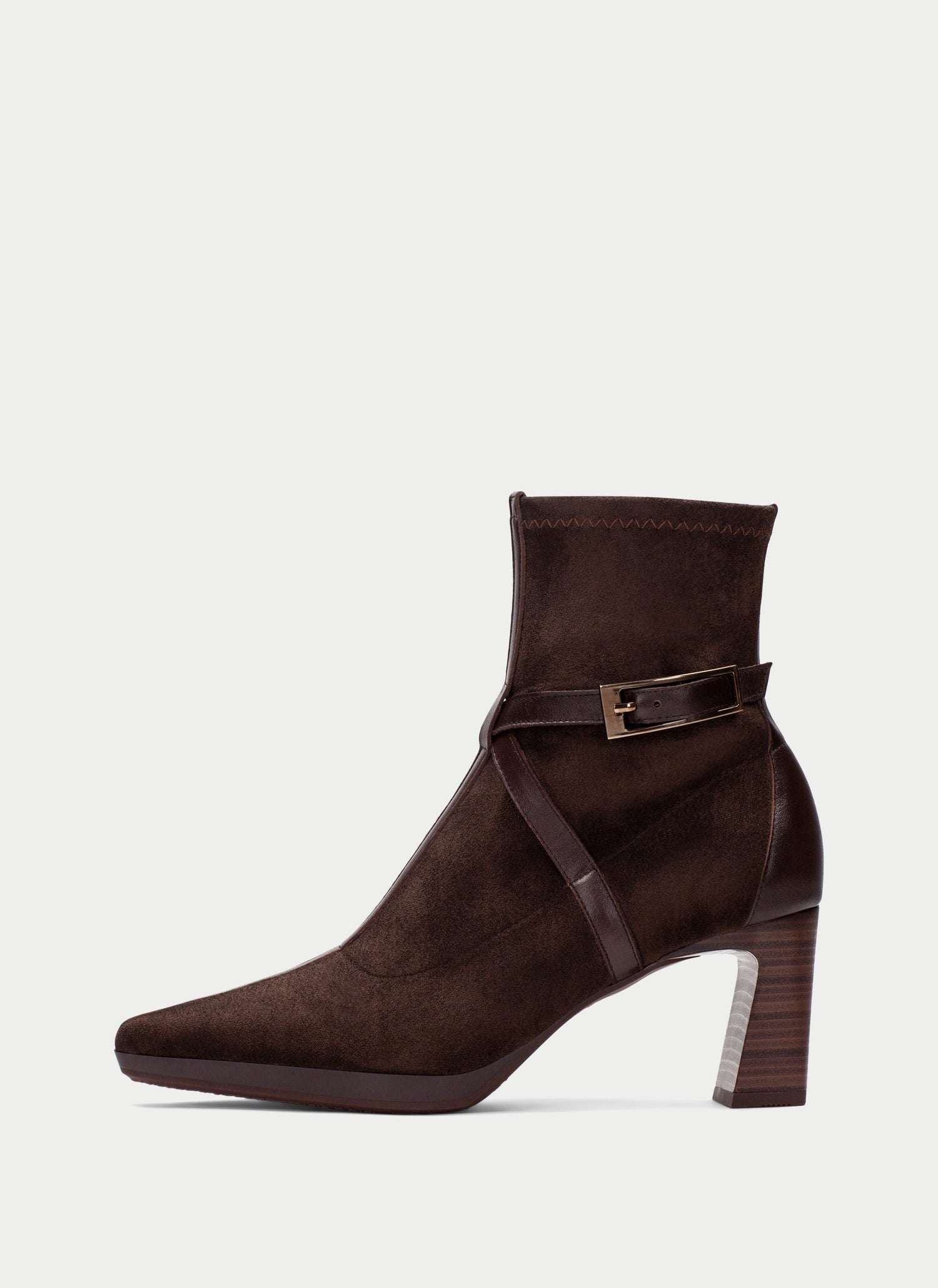 A dark brown suede ankle boot with a pointed toe, a stacked block heel, and a decorative ankle strap with a gold-tone buckle, shown against a light gray background.
