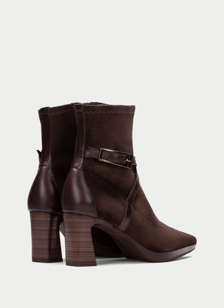 A dark brown suede ankle boot with a pointed toe, a stacked block heel, and a decorative ankle strap with a gold-tone buckle, shown against a light gray background.