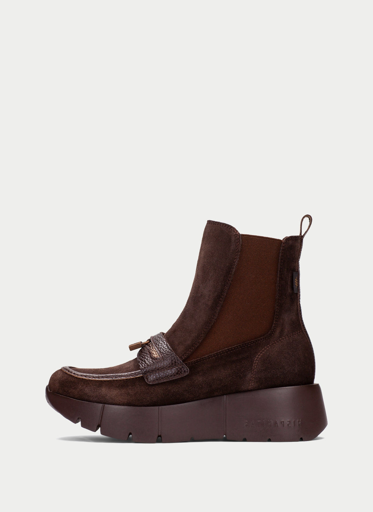 A dark brown ankle boot with a chunky platform sole, featuring a textured leather toe cap with a tassel detail and elastic side panels, shown against a light gray background.