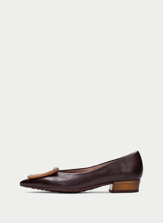 A dark brown leather pointed-toe flat shoe with a low block heel and a tan leather tassel detail on the toe, shown in profile against a light gray background.