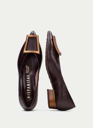 A dark brown leather pointed-toe flat shoe with a low block heel and a tan leather tassel detail on the toe, shown in profile against a light gray background.