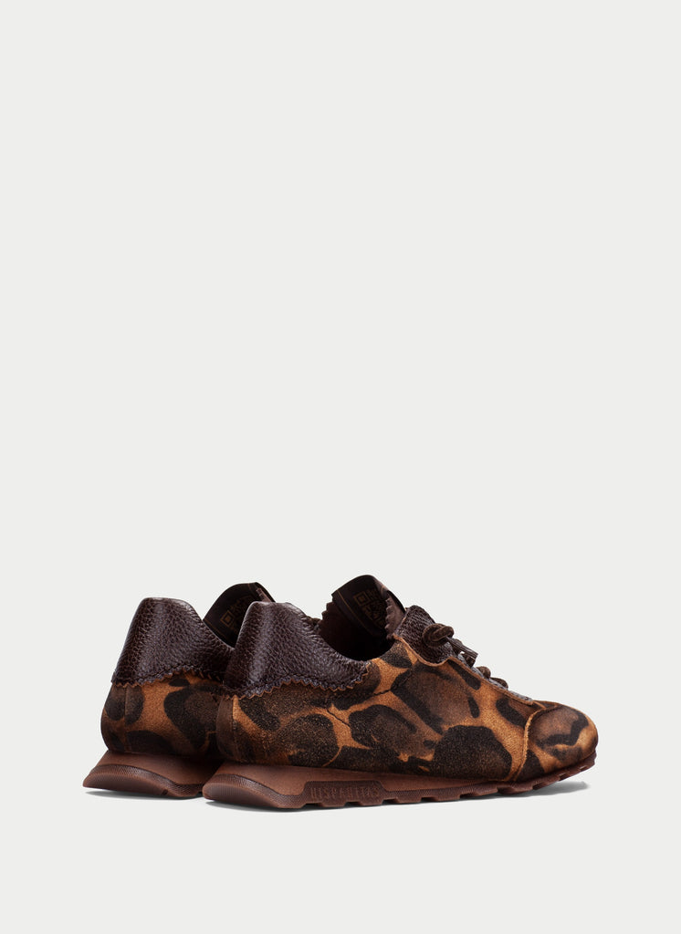 A pair of low-top lace-up sneakers featuring a brown and black leopard print pattern with dark brown leather heel panels, shown from a side profile against a light gray background.