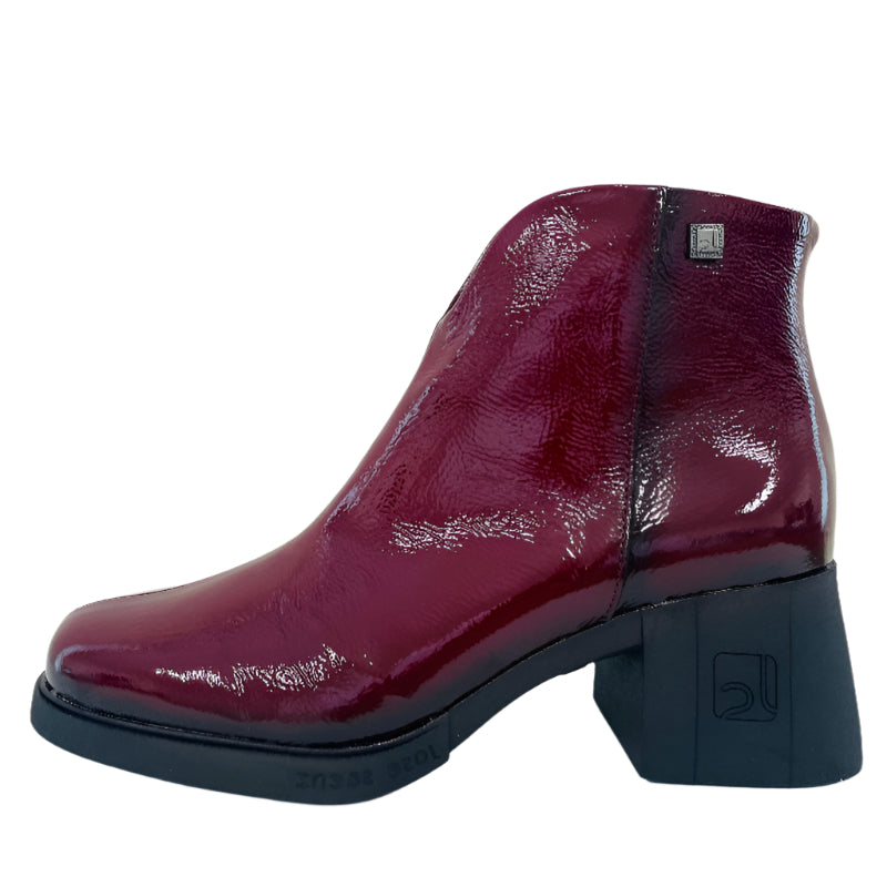Burgundy patent leather boot on a white surface with a light gray wall background