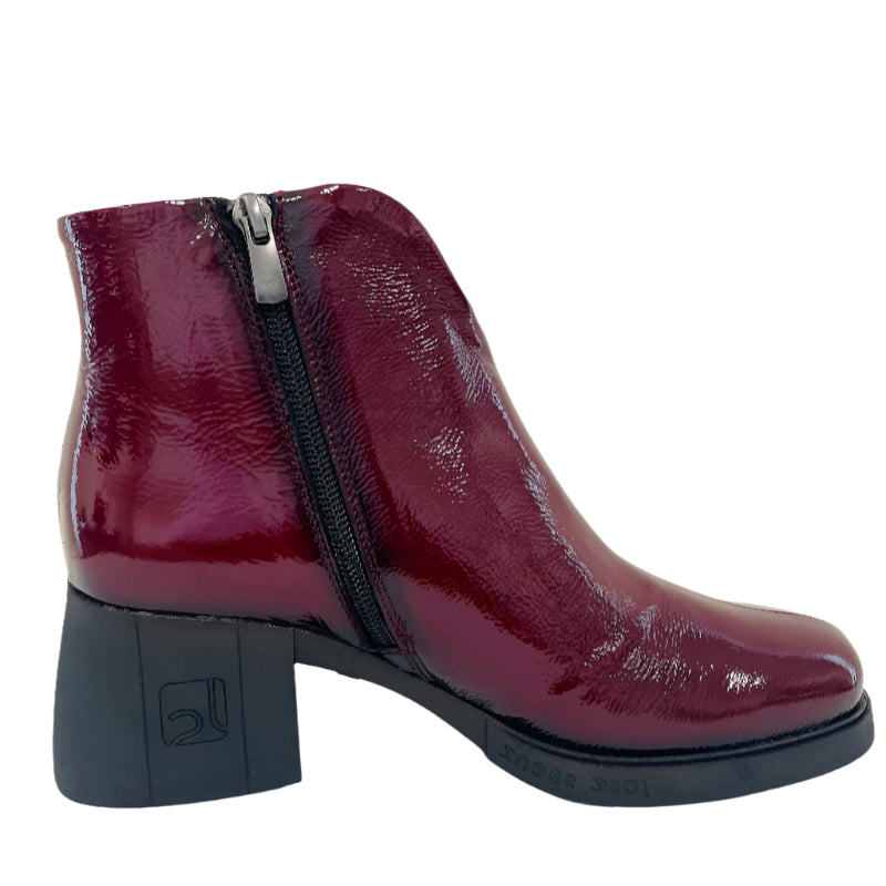 Maroon patent leather ankle boot with a zipper on a white background
