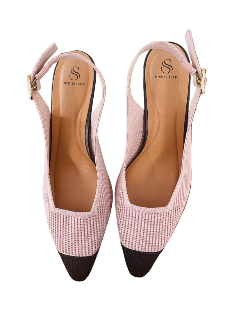 Pair of pink and black shoes on a wooden surface with a tiled wall background