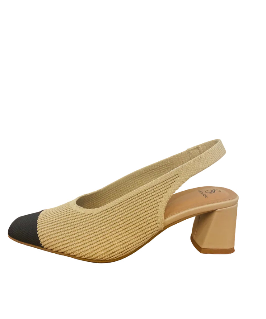 Beige and black heeled shoe on a wooden surface with a white wall background